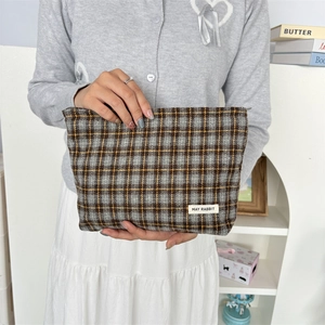 Close-up of a checkered canvas cosmetic bag with zipper and brand tag held by hands