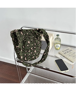 Detail of green plush leopard print bucket bag texture and wide strap on metal shelf