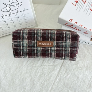 Detail view of the red and green plaid pencil case with a brown leather logo tag