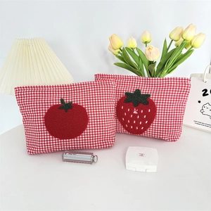 Detail of red checkered cosmetic bags with cute fruit embroidery on a white desk
