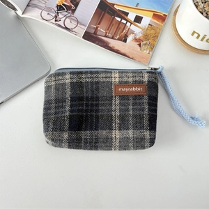 Detail of vintage plaid coin purse featuring a leather logo tag and woven zipper pull