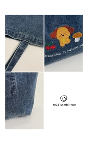 Close-up of embroidered puppy and mushroom patterns on blue denim tote bag