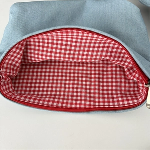 Vue détaillée de la trousse en denim avec fermeture éclair rouge et doublure vichy