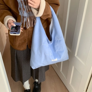 Light blue plush tote bag with bird embroidery being carried in a home setting