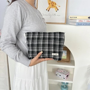 Close-up of checkered canvas makeup pouch held by model in cozy indoor setting