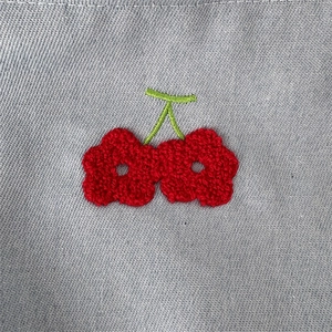 Gros plan sur la texture denim gris avec broderie florale rouge en 3D sur un sac de voyage