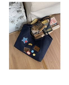 Detailed close-up of dark denim tote bag featuring colorful star, apple and text patches