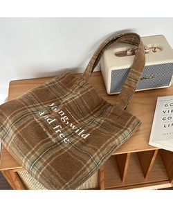 Close-up of brown plaid wool tote bag with embroidered letters on a vintage cabinet