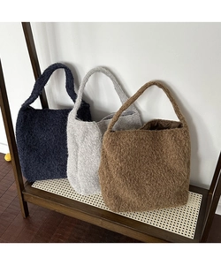 Close-up of three wool bucket bags in blue, grey, and brown on a wooden shelf