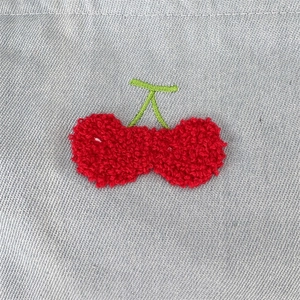 Vue détaillée de la trousse de toilette en jean avec broderie cerise rouge en relief
