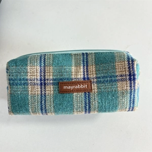 Detailed close-up of blue and green plaid tweed pencil case with a brown leather label