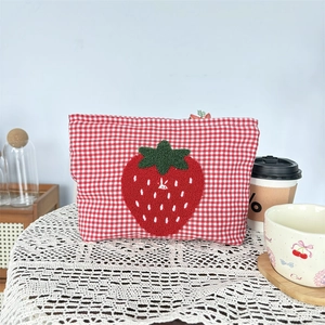 Close-up of red checkered makeup bag featuring a textured chenille strawberry embroidery
