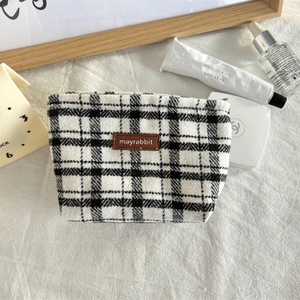Detail van zwart-wit geruite tweed make-uptas met lederen logo op een crème achtergrond