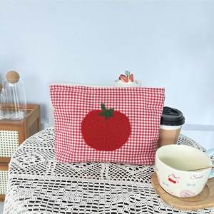 Red checkered makeup bag with embroidered tomato design on a white lace tablecloth