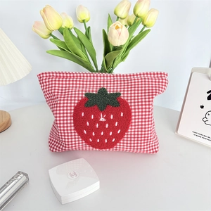 Detail of red checkered toiletry bag featuring 3D strawberry embroidery and fabric texture