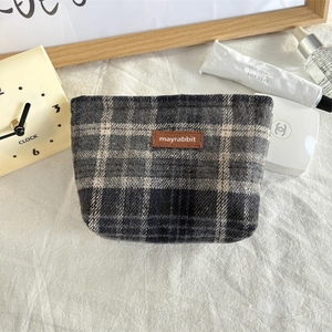 Detailopname van de grijze ruitvormige cosmetische tas met een lederen merklabel erop