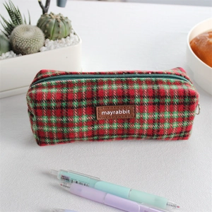 Detail of red and green plaid wool pencil case featuring a brown leather logo and zipper