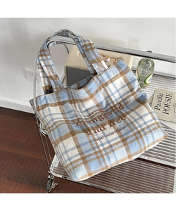 Detail of blue and brown plaid tote bag featuring embroidered text in a cozy home setting