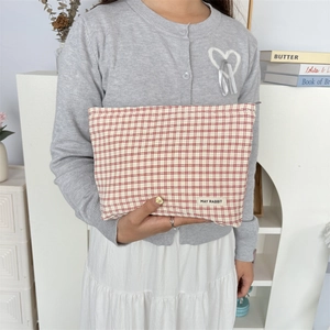 Rood-wit geblokte stoffen make-up tas vastgehouden door model in minimalistisch décor