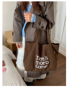 Deep brown canvas tote bag with artistic letter print shown in a lifestyle scene