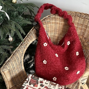 Nahaufnahme der roten Plüschtasche mit weißen Blumenapplikationen auf einem Holzstuhl