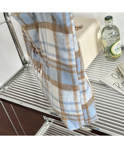 Detail of blue and brown plaid wool tote bag with embroidered letters on a metal shelf