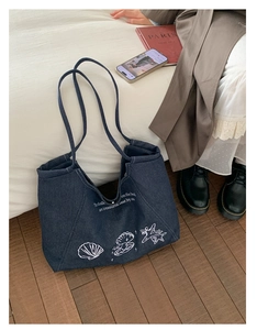 Detail of blue denim tote bag featuring white sea shell prints and artistic text