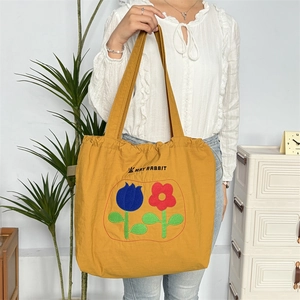 Gelbe Kordelzug-Einkaufstasche mit Tulpen-Stickerei und May Rabbit-Logo am Modell getragen