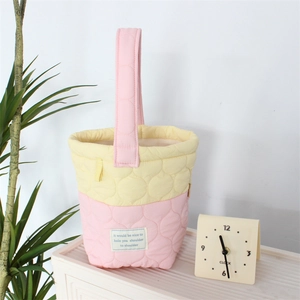 Detail of pink and yellow quilted bucket bag with slogan patch on a white striped surface