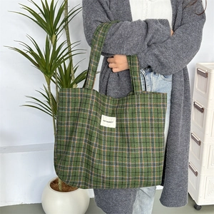 Détail du grand sac cabas en laine à carreaux verts et orange avec un écusson logo
