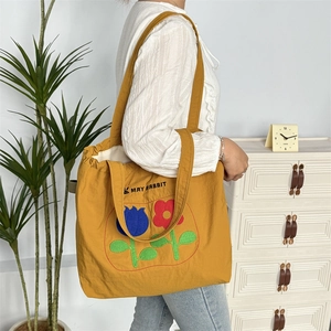 Detail einer großen gelben Beuteltasche mit Blumenstickerei und praktischen Schultergurten