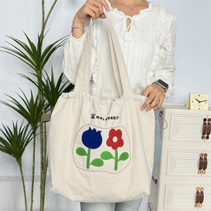 Nahaufnahme der Blumenstickerei und Kordelzugdetails an der cremefarbenen Canvas-Tasche
