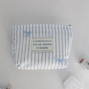 Detail of blue striped makeup pouch featuring embroidered bows and a metal zipper