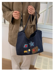 Close-up of dark denim tote bag with colorful star, apple, and button patches