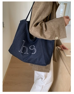 Detail of blue denim tote bag with h9 lettering worn on the shoulder in a warm setting