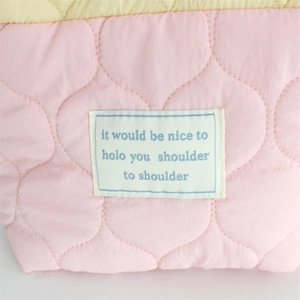 Close-up of pink quilted heart bag with yellow trim and embroidered woven patch detail