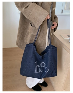 Detail shot of navy denim tote bag with ho letter embroidery on shoulder strap