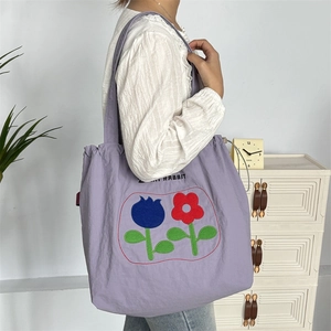 Detailansicht der lila Kordelzug-Einkaufstasche mit Blumenstickerei am Schultergurt