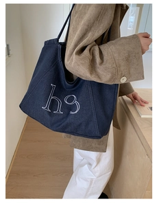 Detail of deep blue denim tote with h9 logo styled with a brown coat in indoor setting
