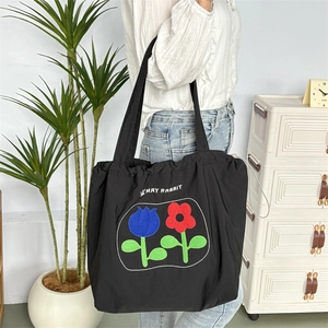 Detailansicht der schwarzen Nylon-Kordelzug-Tasche mit Blumenmuster und breitem Schultergurt