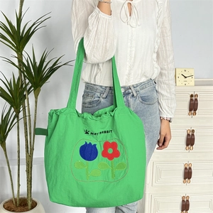 Detail der grünen Canvas-Tasche mit May Rabbit-Logo und Blumenstickerei auf der Schulter