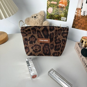 Close-up of suede leopard print cosmetic bag with brand patch on a stylish desktop