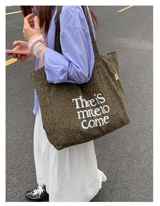Detail view of leopard print canvas tote bag featuring white artistic slogan and logo tag