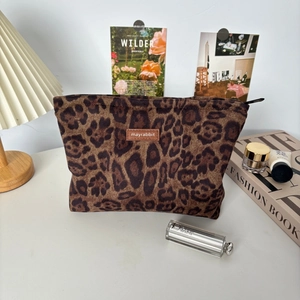 Close-up of vintage leopard print suede makeup bag with leather logo tag on a desk