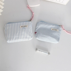 Detail of blue striped makeup pouches with pink pull cords on minimalist background