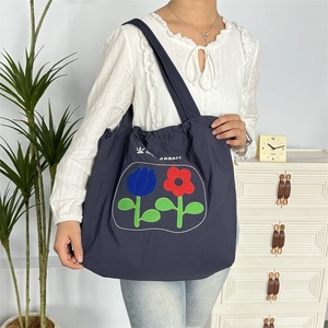 Nahaufnahme der dunkelblauen Kordelzug-Tasche mit Blumenstickerei und Hasen-Logo-Detail