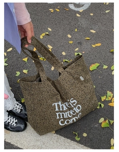Detail of leopard print canvas tote bag with 'There is more to come' text in autumn setting