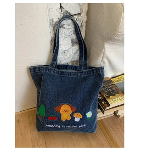 Detailed close-up of embroidered puppy and nature motifs on dark blue denim tote bag