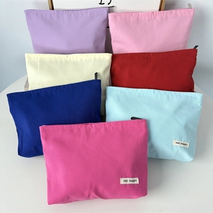Stack of colorful canvas makeup bags with zip closure and minimalist logo labels
