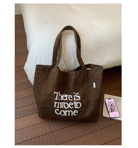 Close-up of deep brown canvas tote bag with white letter print and textured fabric detail